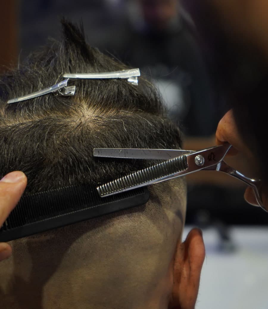 A barber cutting a client’s hair with scissors and a comb