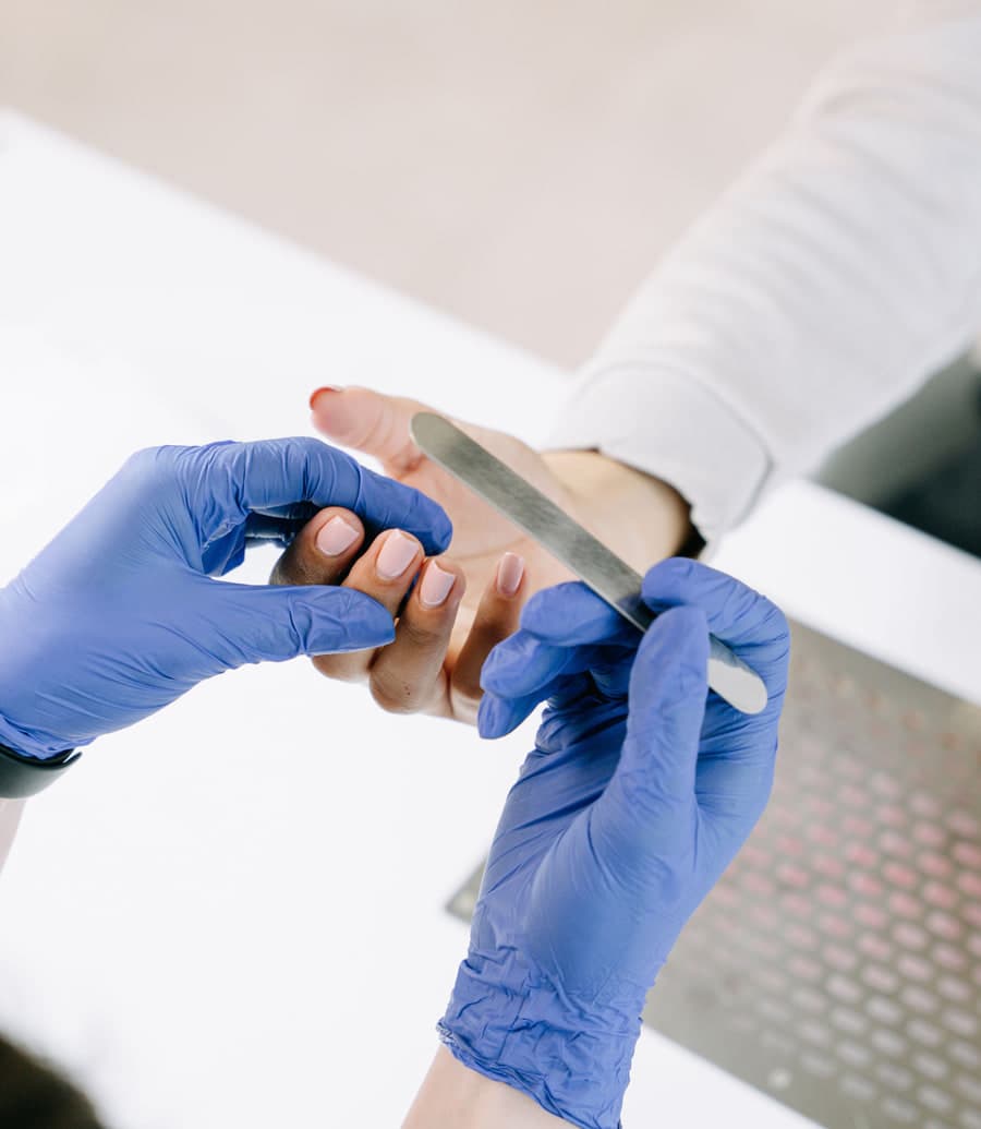A gloved nail technician filing a client’s nails