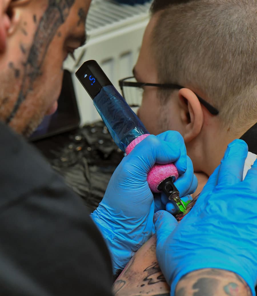 A gloved tattoo artist working on a client’s shoulder